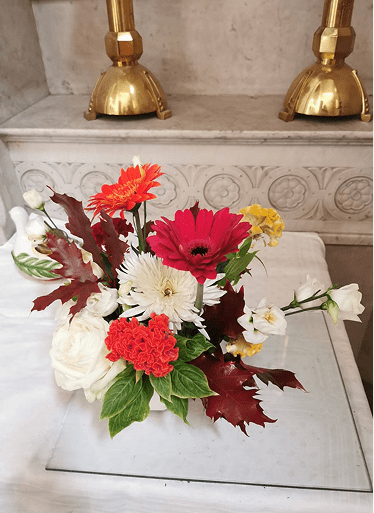 Composition florale avec gerberas rouges et oranges, fleurs blanches et feuillage pourpre.