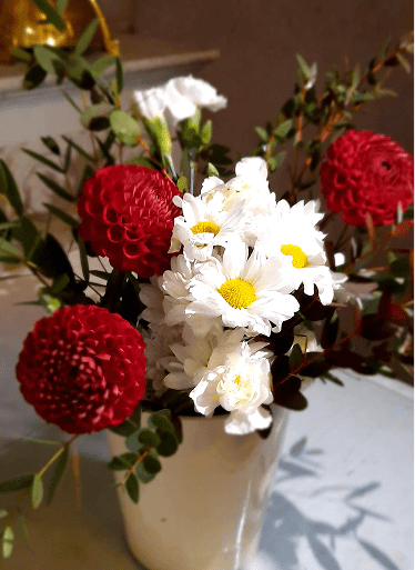 Bouquet champêtre composé de dahlias rouges et de marguerites blanches dans un vase clair.