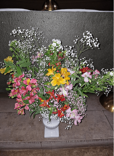 Grand bouquet léger disposé dans un vase sur pied blanc, composé d'un nuage de gypsophile, d'alstroemérias (lys des Incas) roses, jaunes et rouges.