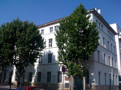 Bâtiment blanc de l'école de la Rédemption bordé d'arbres feuillus sous un ciel bleu.