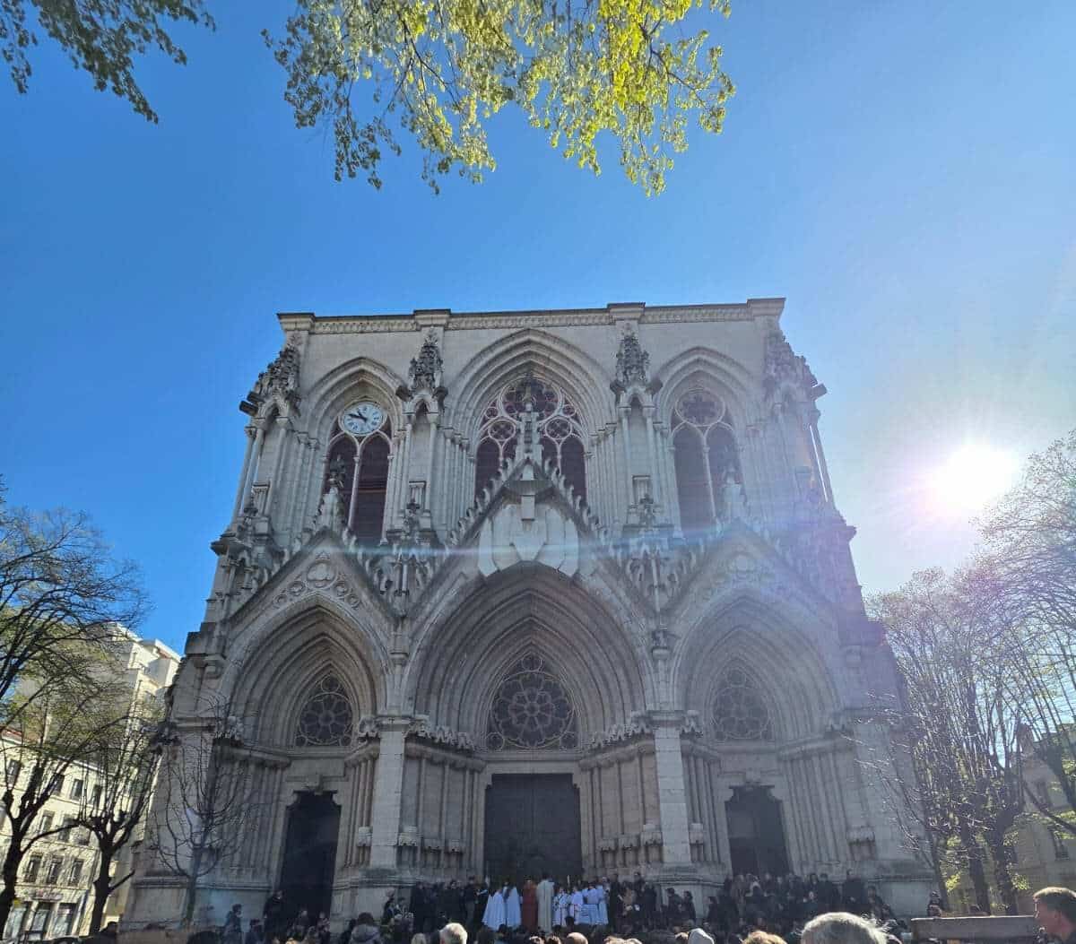 Rassemblement de fidèles devant l'entrée de l'église de la Rédemption sous un ciel ensoleillé.